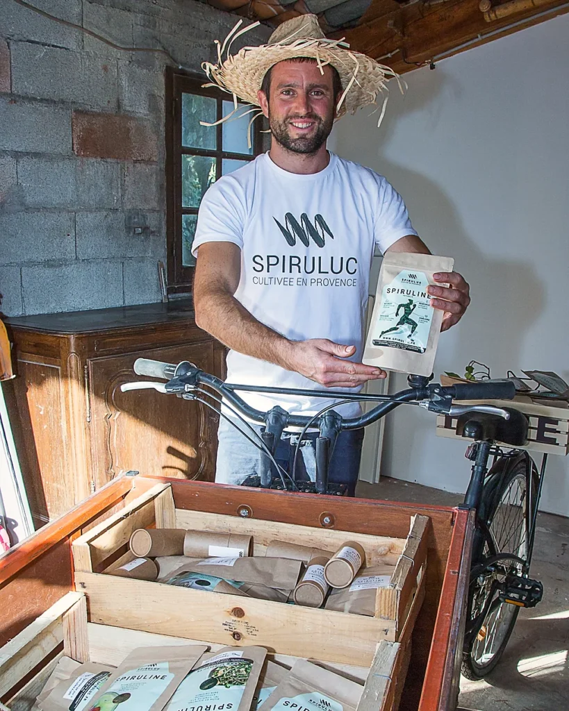 Boris présente un sachet de spiruline avec son vélo cargo, vente directe à la ferme du Luc
